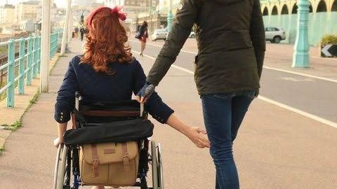 Woman on a skateboard pushes a woman in a wheel chair