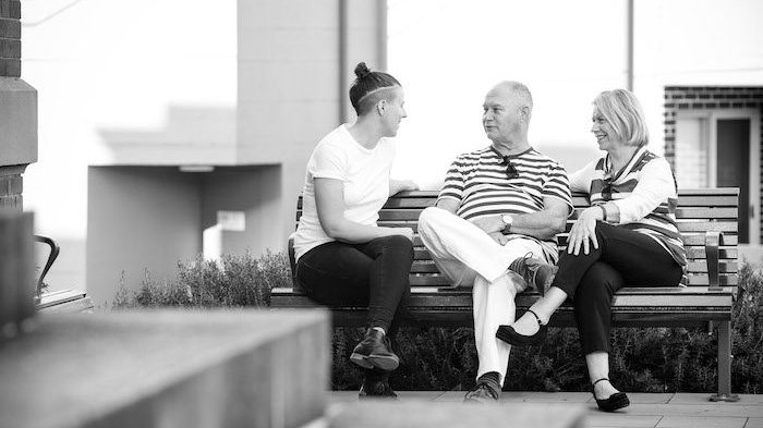 Black and white picture of 3 people sitting on a bench talking