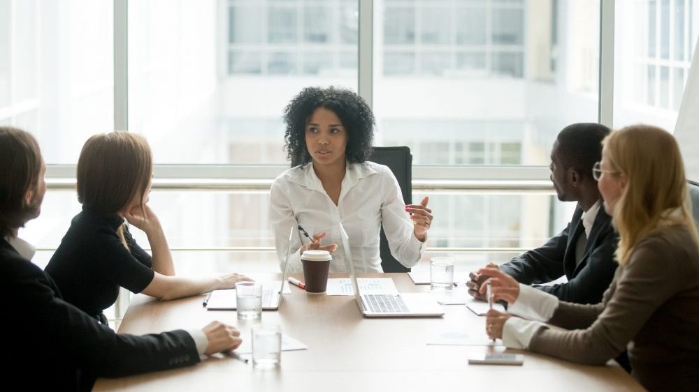 Woman of colour sitting at head of boardroom table talking