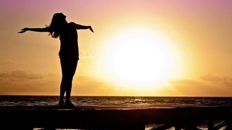 woman welcoming sunrise with open arms