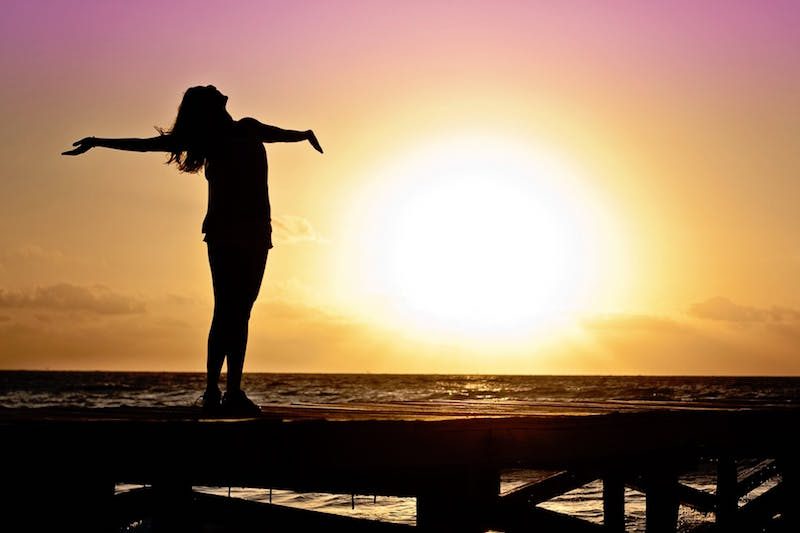 woman welcoming sunrise with open arms