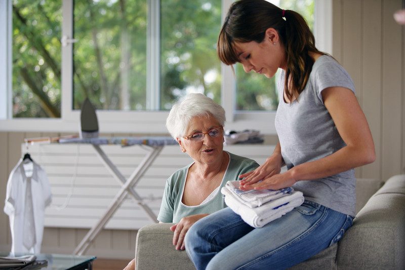 A younger woman folding laundry for an older woman