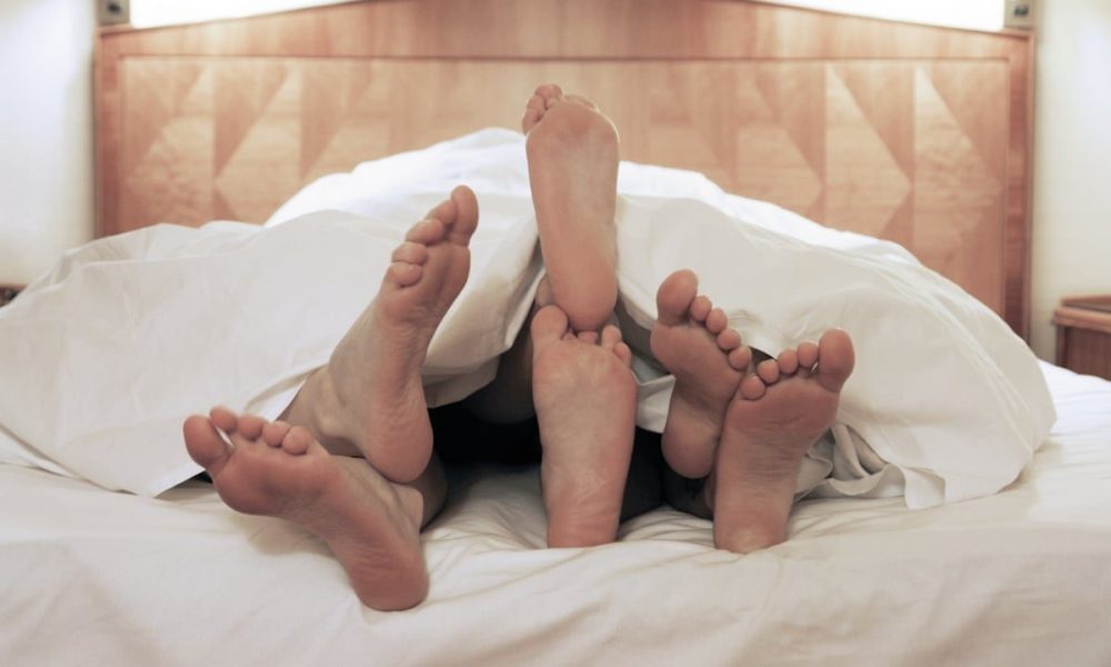 3 pair of feet sticking out at the end of a bed