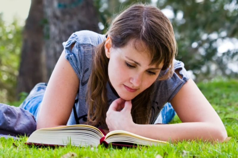 female lying on grass reading book 
