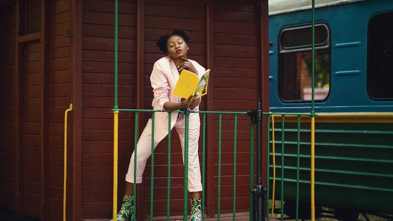 black woman reading book next to a train