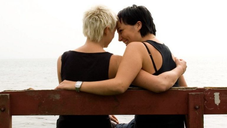 2 women sitting on bench by the water