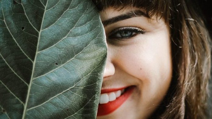 smiling women looking from behind large leaf